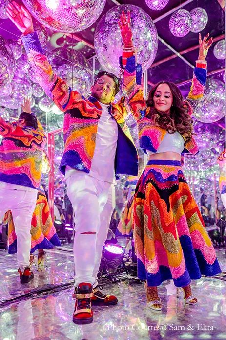 a man and woman in colorful outfits dancing on stage with disco balls hanging from the ceiling