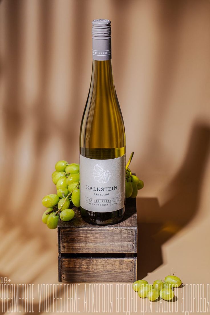 a bottle of wine sitting on top of a wooden crate next to some green grapes