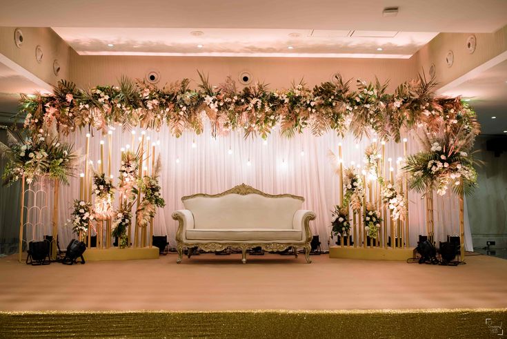 a couch sitting on top of a stage covered in flowers and greenery next to a wall