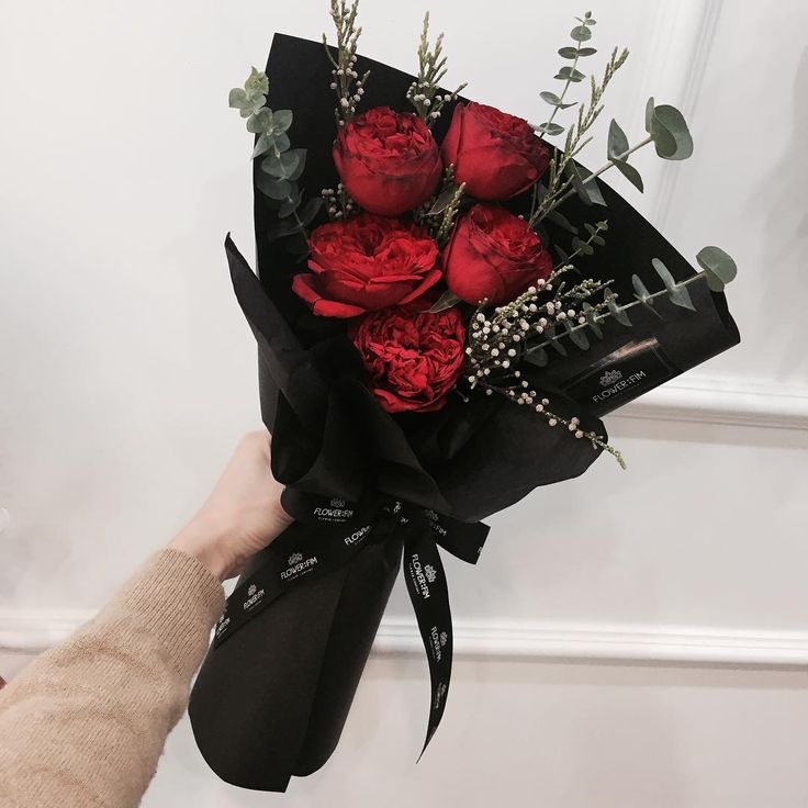 a hand holding a bouquet of red roses and greenery in black paper wrapped around it