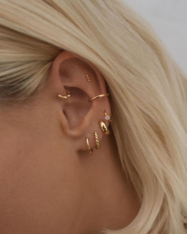 a woman with blonde hair wearing three gold ear cuffs and an earring that is shaped like a leaf