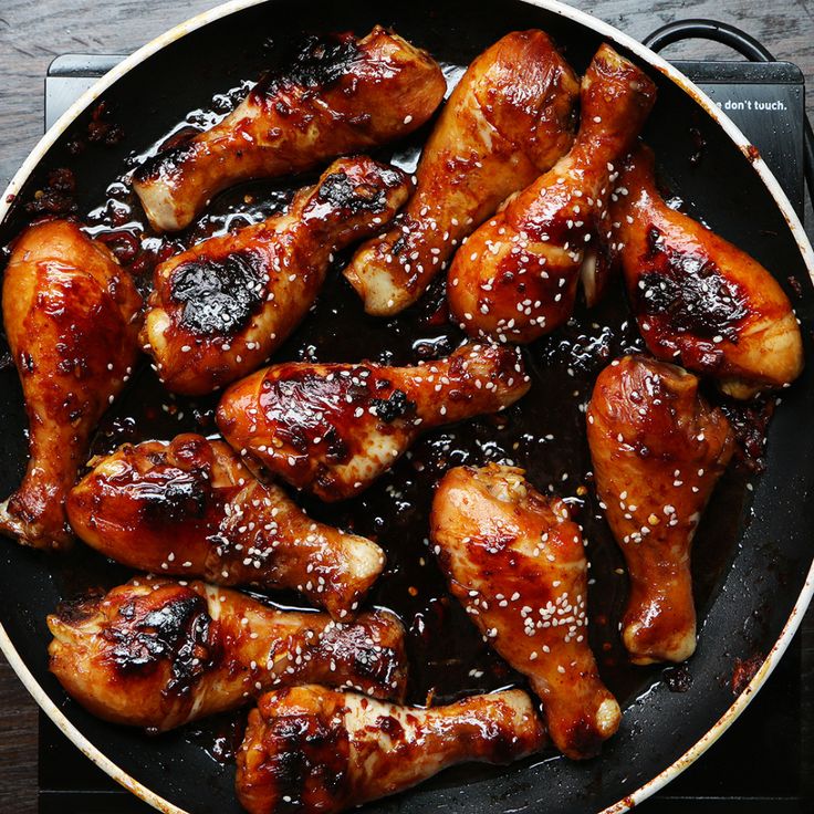 chicken wings are cooking in a skillet with sesame seeds on the side and teriyaki sauce