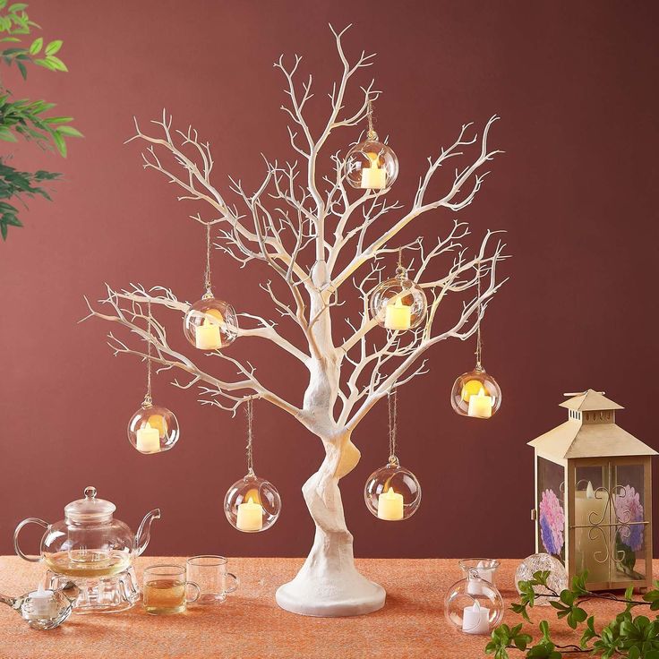 a white tree with ornaments hanging from it's branches on a table next to a potted plant