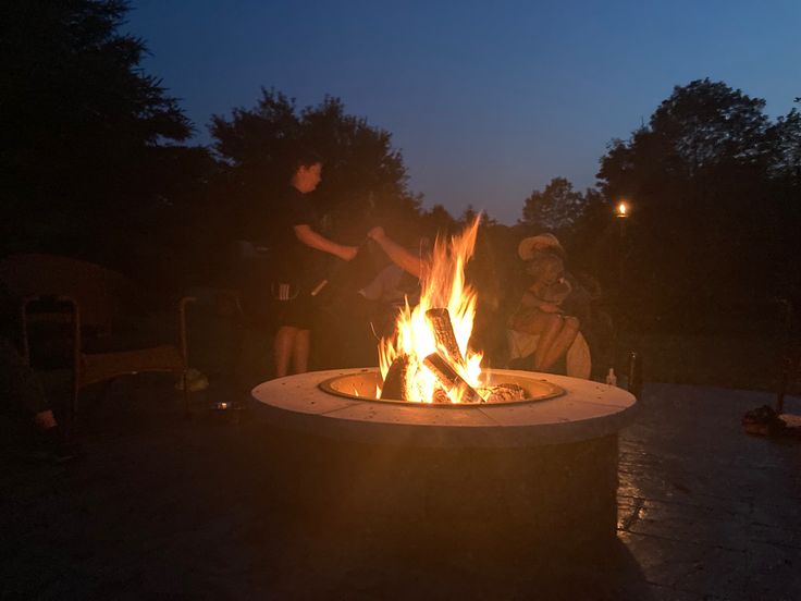 three people sitting around a fire pit at night