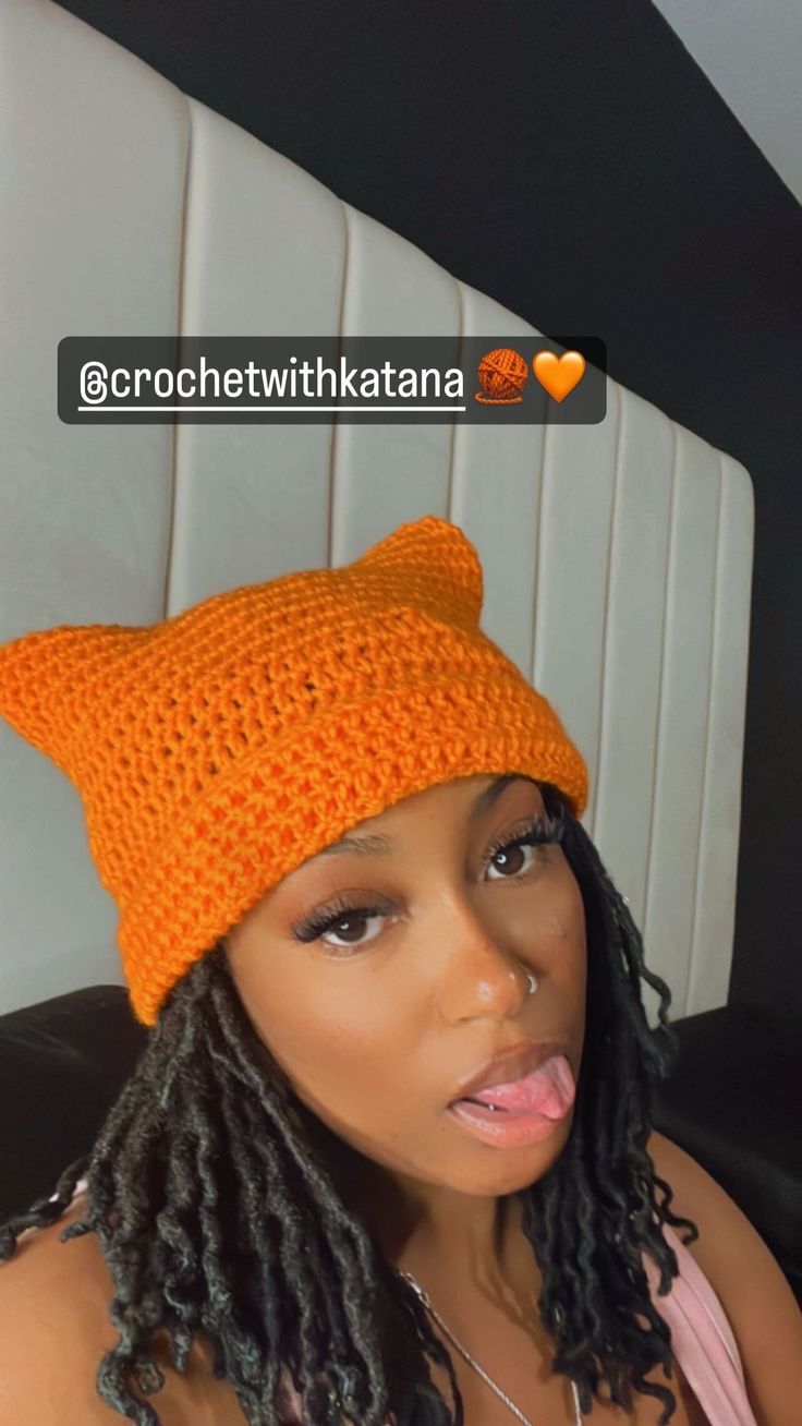 a woman wearing an orange knitted cat hat with dreadlocks on her head