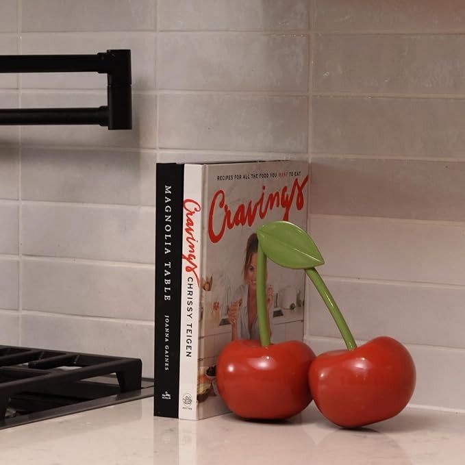 two cherries sit on the counter next to a cookbook, and a stove