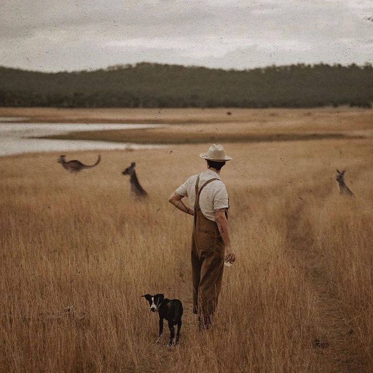 a man standing in the middle of a field next to a dog