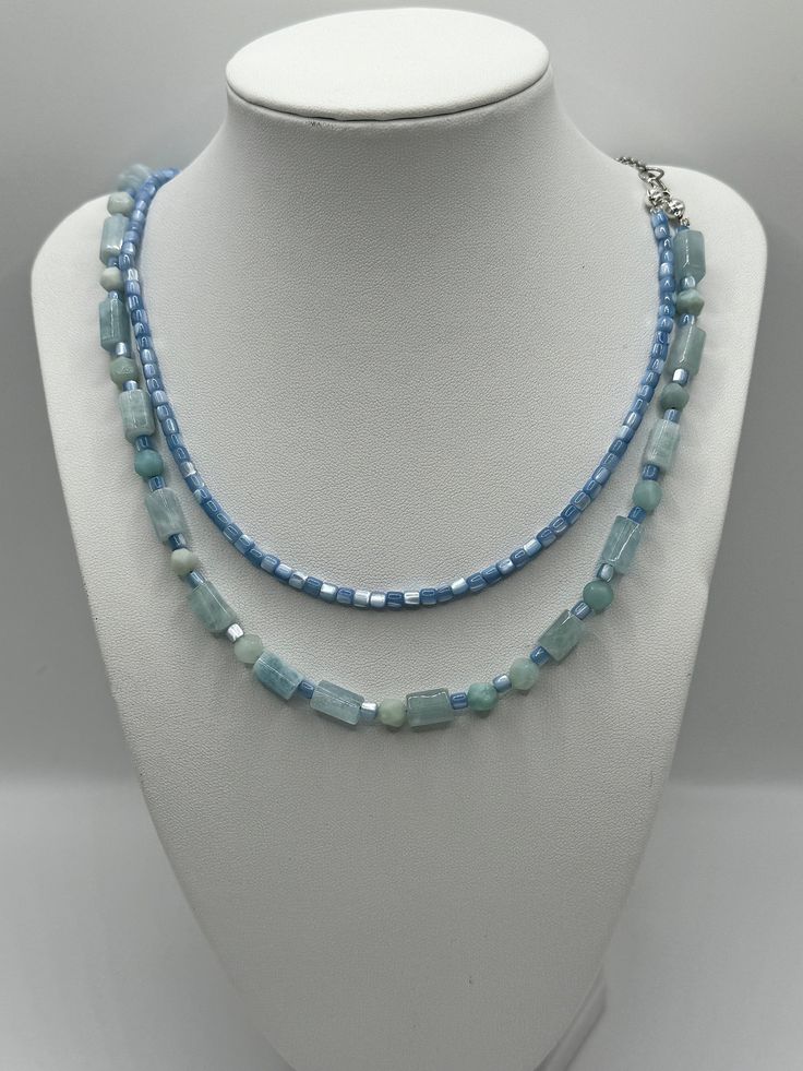 This elegant display a duo of features a serene blue  necklaces, each presenting a unique shape and size of bead, creating a symphony of sky and sea hues.  The first strand (small) features natural shell beads and the  larger cylindrical tube beads are aquamarine . The longest necklace presents a harmonious blend of spherical and tubular beads, lending a dynamic and versatile appearance. Together, they form a layered cascade of tranquil blues, perfect for adding a touch of sophistication and coo Light Blue Single Strand Necklace With Round Beads, Light Blue Multi-strand Jewelry As Gift, Light Blue Multi-strand Jewelry Gift, Light Blue Multi-strand Jewelry For Gift, Elegant Light Blue Necklaces With Natural Stones, Elegant Light Blue Necklace With Natural Stones, Light Blue Single Strand Jewelry For Jewelry Making, Blue Single Strand Long Beaded Necklace, Blue Long Single Strand Beaded Necklace