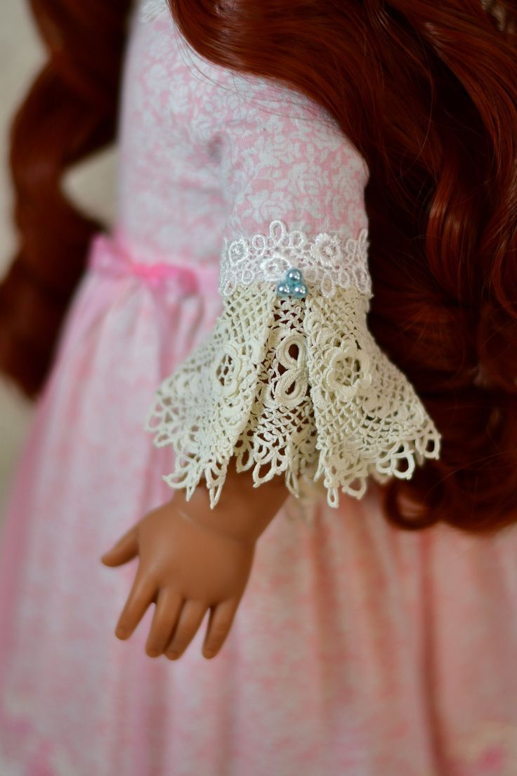 a doll with red hair wearing a pink dress and white lace on it's arm