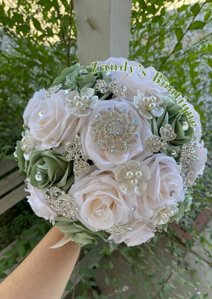 a bridal bouquet with white roses and green leaves is held by someone's hand