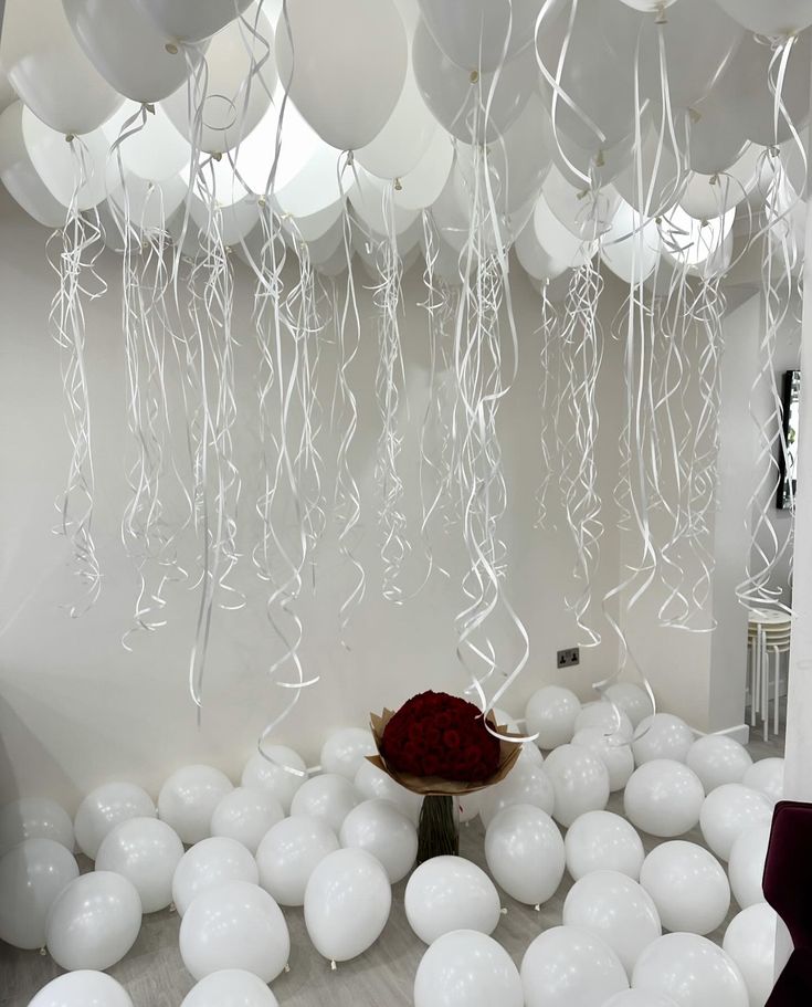 balloons and streamers hang from the ceiling in a room with an arrangement of flowers