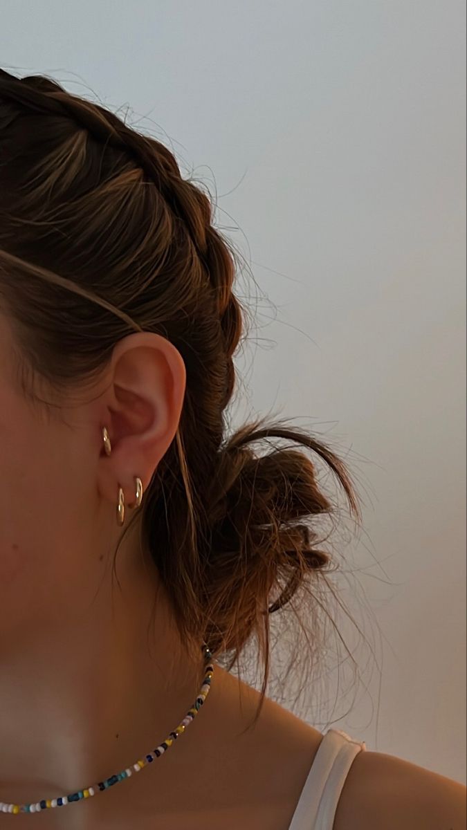 a woman wearing a necklace and earring next to a white wall with her hair in a bun