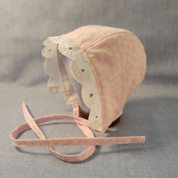 Made to Order. Crafted with love and care from 100% cotton and eyelet lace trim, this handmade cotton baby bonnet is a charming accessory for your little one. Made from soft, breathable cotton, it ensures comfort and style in one adorable package. The delicate craftsmanship of this bonnet adds a touch of artisanal flair to your baby's ensemble. Whether worn for a special occasion or as a daily accessory, this bonnet is both practical and delightful. Its timeless design and high-quality materials make it a thoughtful gift for new parents or a sweet addition to your baby's wardrobe. Add a touch of handmade beauty to your baby's look with this lovely cotton baby bonnet. Perfect for protecting your baby's delicate skin from the sun or wind, this bonnet is as functional as it is adorable. The a White Cotton Bonnet As A Gift, White Cotton Bonnet As Gift, Adjustable Cotton Bonnet With Lace Trim, Handmade Cute Pink Bonnet, Cute Handmade Pink Bonnet, Pink Cotton Bonnet For Spring, Cute Pink Cotton Bonnet, Adjustable Cotton Vintage Bonnet, Fitted Cotton Bonnet With Lace Trim