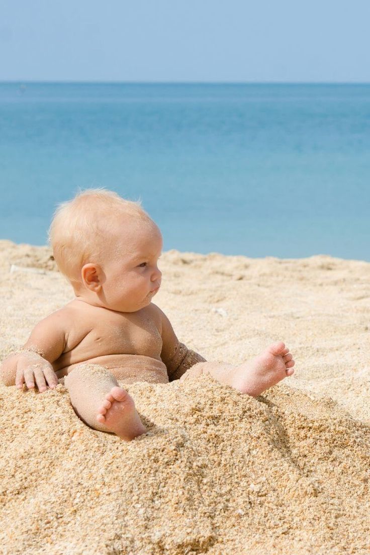 a baby sitting in the sand at the beach