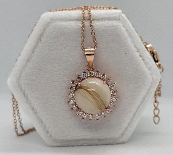 a white and gold necklace with an oval shaped stone in the center on a chain