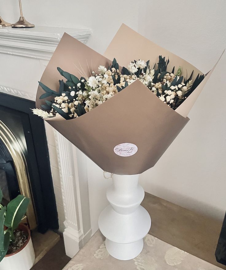 a bouquet of white flowers in a brown paper bag on a table next to a fireplace