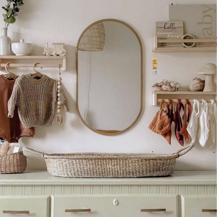 a white dresser topped with a mirror and a wicker basket filled with baby clothes