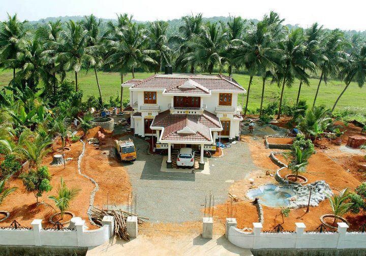 an aerial view of a house in the middle of palm trees and dirt area with cars parked outside