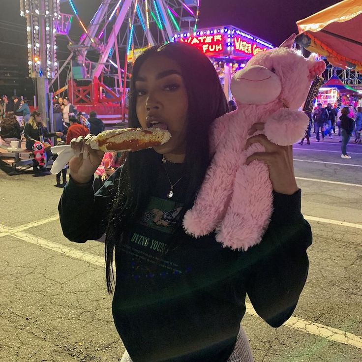 a girl eating pizza at an amusement park with a pink stuffed animal on her shoulder