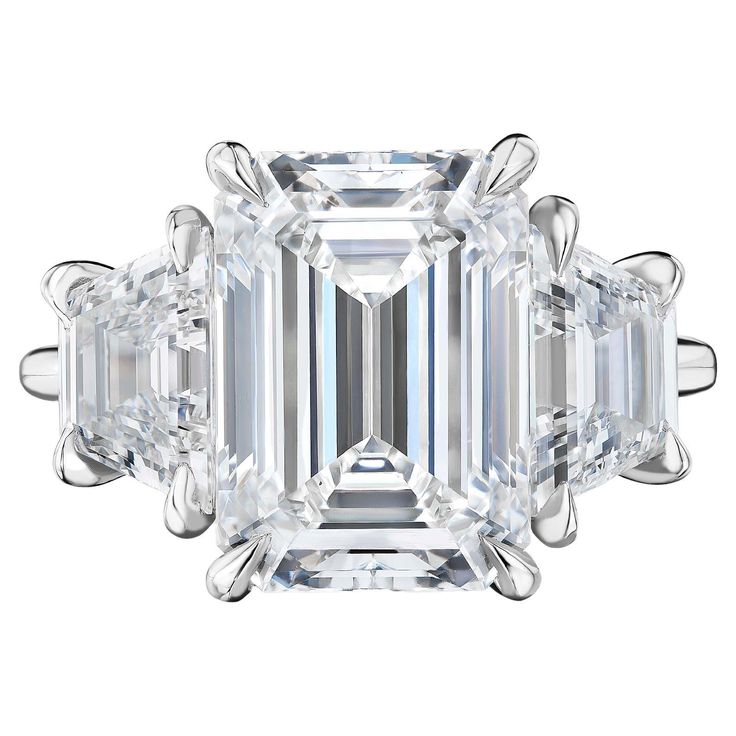 an emerald - cut diamond ring with three baguets on the side and four clawed shoulders