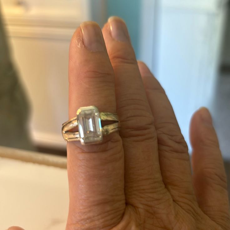 a woman's hand holding a ring with an emerald stone in the middle and a diamond on the side