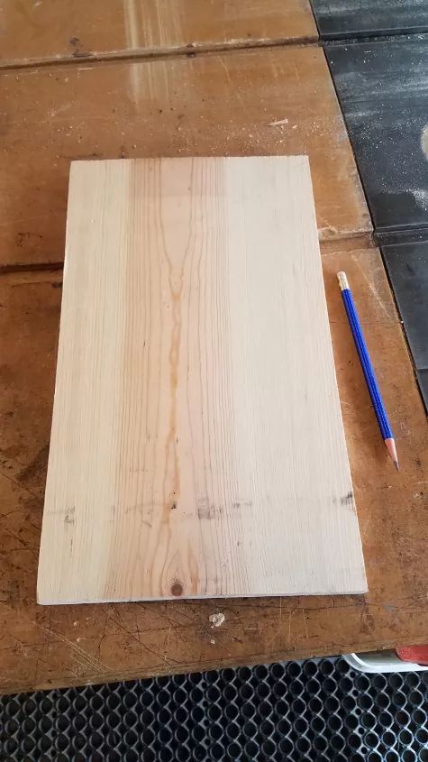 a piece of wood sitting on top of a wooden table next to a blue pen