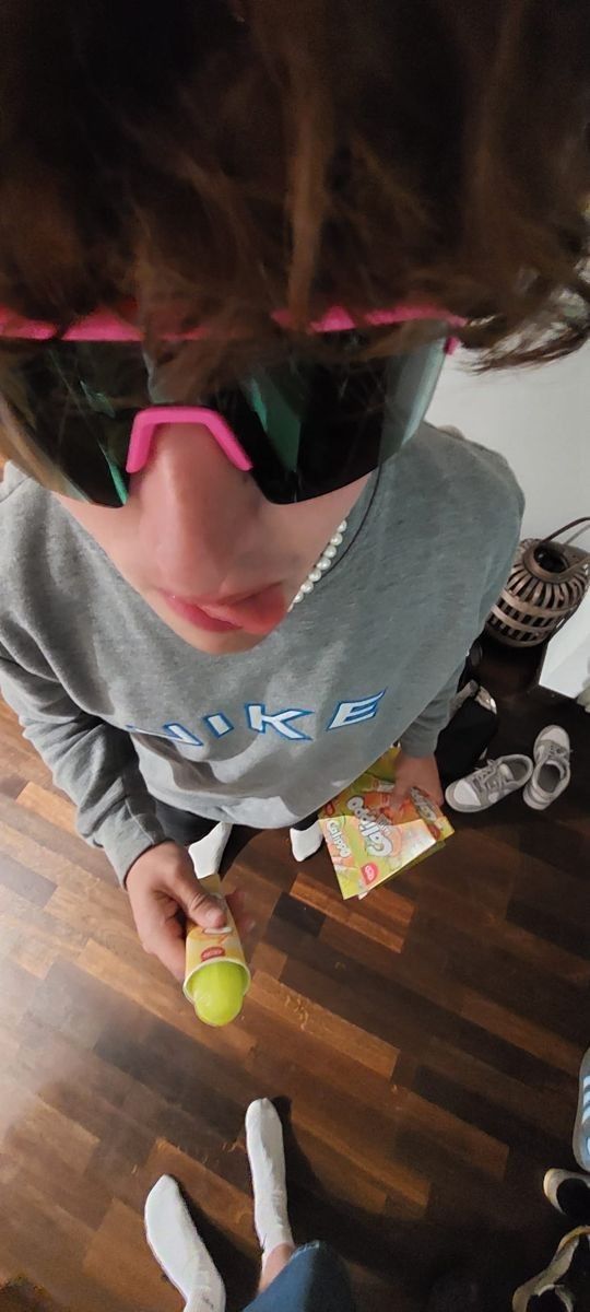 a person wearing sunglasses and holding a tennis ball in front of their face while standing on a hard wood floor