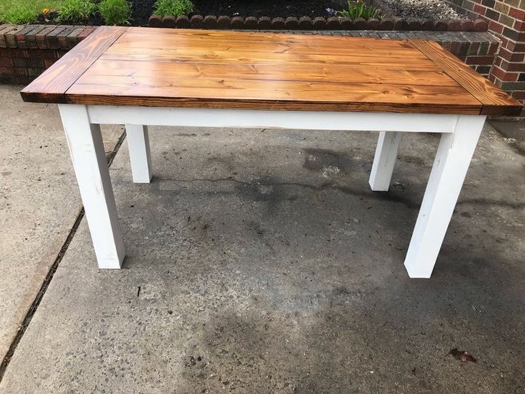 a white and wood table sitting on top of a cement ground next to a brick wall