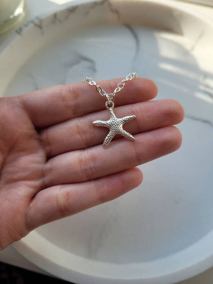 Silver plated starfish charm attached to an 18inch silver plated sparkle chain necklace with lobster claw closure. The charm is attached to the necklace via a silver plated jump ring. The charm measures 1.9cm long x 1.9cm wide. The necklace measures 18inches. This super cute starfish necklace is a great reminder of times spent near the seaside. The necklace will come gift wrapped in tissue paper and an organza bag. Please note that although I have endeavour to show of my pieces in the best, natu Star Jewelry With Lobster Clasp, Ocean-inspired Pendant Necklace With Lobster Clasp, Adjustable Silver Charm Necklaces With Star Charm, Ocean-inspired Silver Charms Jewelry, Beach Starfish Charms Necklaces, Star Charm Necklace For Beach, Beach Charms Starfish Necklace, Adjustable Starfish Charm Jewelry, Star Charm Necklaces For Beach