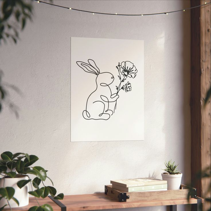 a black and white drawing of a rabbit holding a flower on a wall above a table