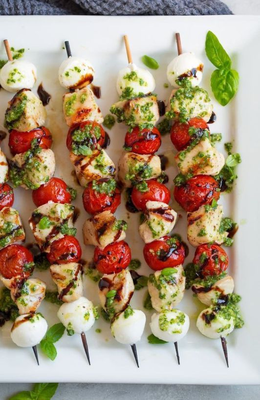 several skewers of meat and vegetables on a white platter with basil leaves