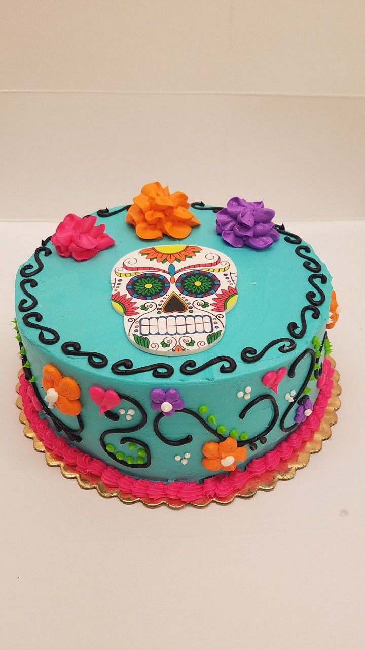 a cake decorated with flowers and a colorful sugar skull on the top is sitting on a table