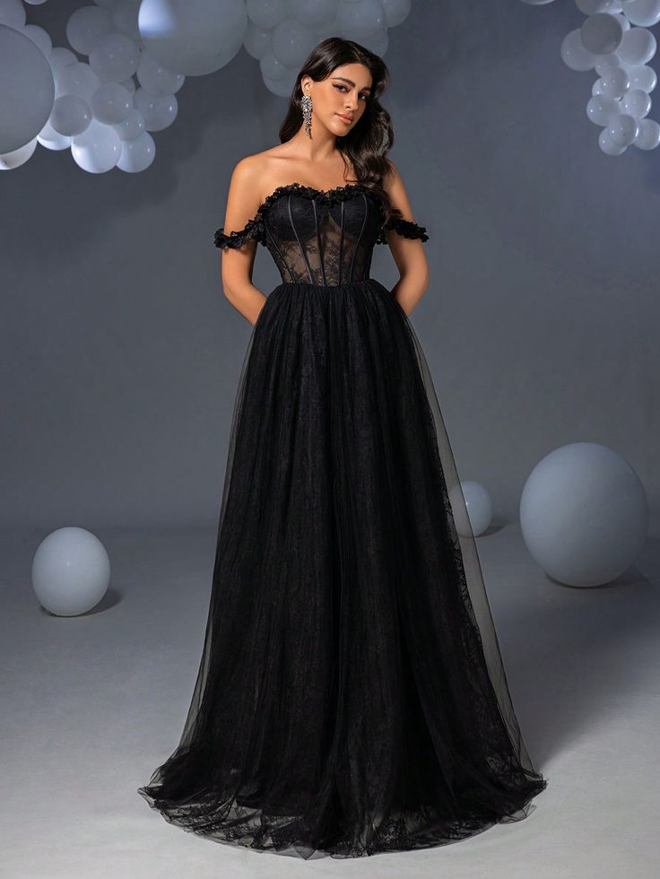 a woman standing in front of balloons wearing a black dress with sheer shoulders and an off the shoulder neckline