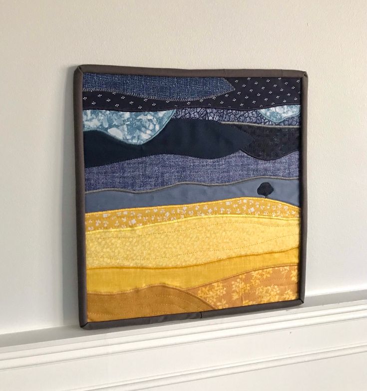 a piece of art hanging on the wall next to a white fireplace mantel with a blue, yellow and black patchwork design