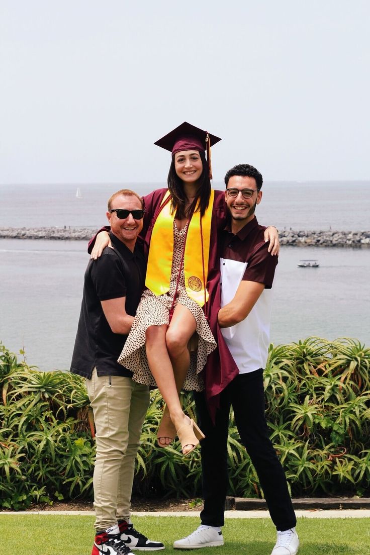 two men and a woman in graduation gowns pose for a photo with a graduate