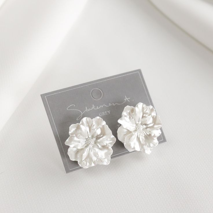 pair of white flower clip earrings on card for sale in store window display, closeup