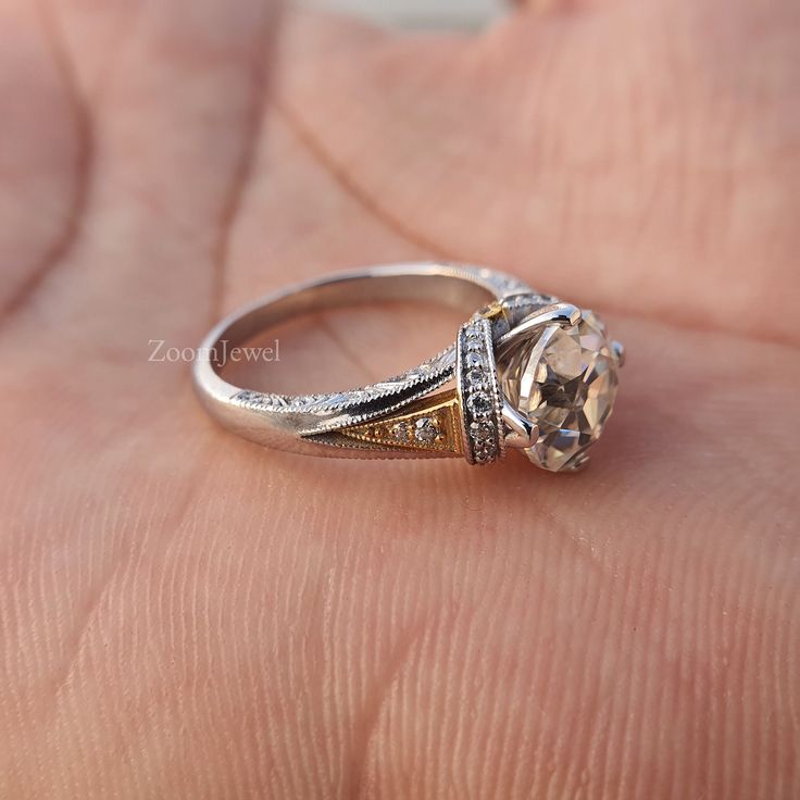 a close up of a person's hand holding an engagement ring with a brown and white diamond