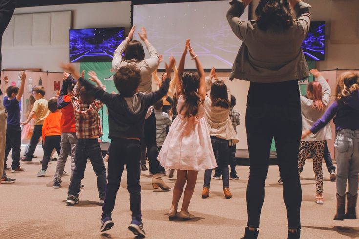 a group of children and adults dancing in front of a projector screen with their hands up