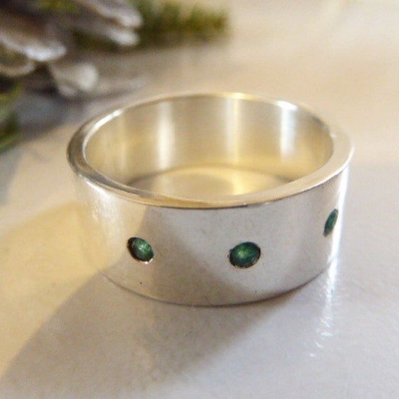 a silver ring with green stones sitting on top of a white table next to flowers