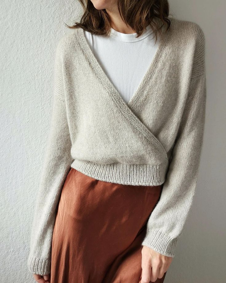 a woman standing in front of a wall wearing a white sweater and brown skirt with her hands on her hips