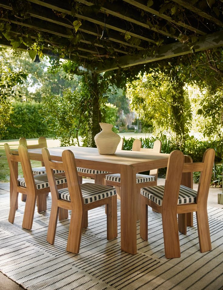 a table and chairs on a deck under an awning with trees in the background