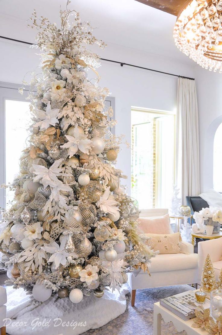 a white christmas tree in a living room decorated with gold and silver ornaments, snowflakes and other holiday decorations