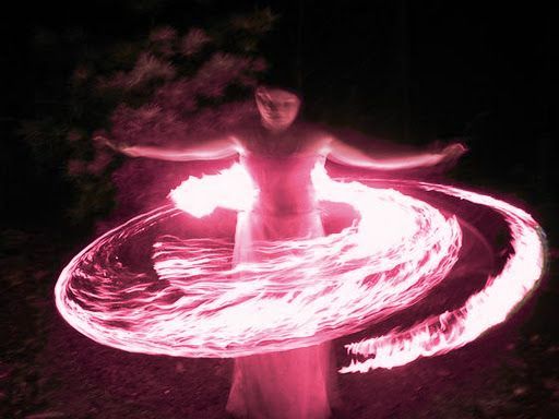 a woman standing in the dark with fire spinning around her