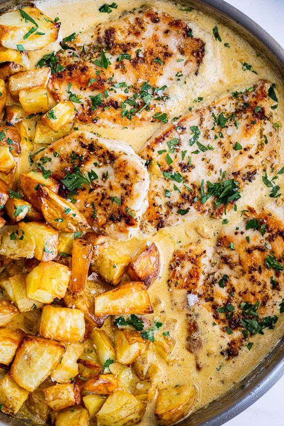 a pan filled with chicken, potatoes and parsley on top of a white table