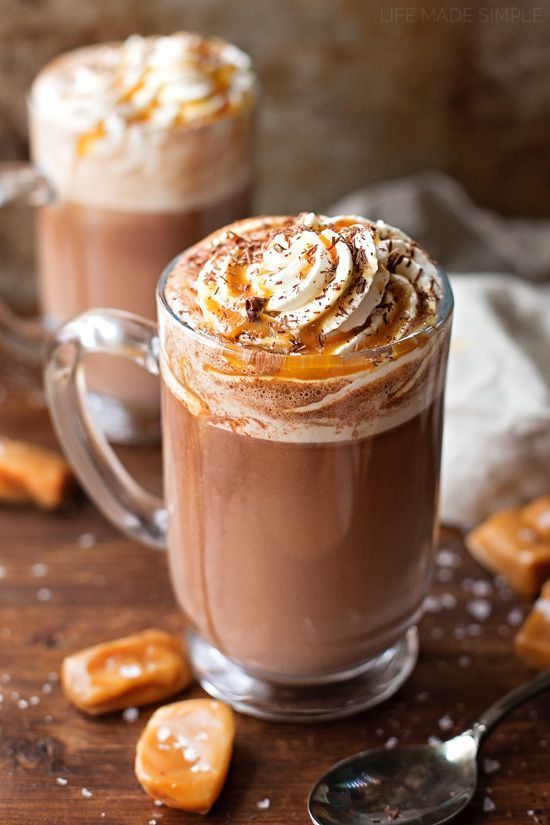 two glasses of hot chocolate with whipped cream and caramel toppings on a wooden table