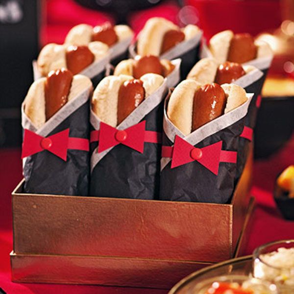 hotdogs wrapped in black paper with red bows are sitting on a gold plate