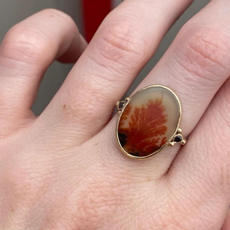 It almost looks like a reef on fire trapped in this Black and Orange Dendrite agate. set in 14k yellow gold bezel with sterling silver back this one of a kind beauty is finished with Emily's 14k gold seagrass band. Approximate stone size: 17mm x 13mm Approx ct weight: 4.4cts Mohs Hardness scale: 7 This one of a kind piece is handmade with love in Emily's Hudson Valley studio. If you have questions about sizing, shipping or need help deciding on your perfect piece please reach out to us! Yellow Gold Oval Agate Jewelry, Oval Agate Yellow Gold Jewelry, Oval Yellow Gold Agate Jewelry, Oval 14k Gold Nature-inspired Jewelry, 14k Gold Nature-inspired Oval Jewelry, Nature-inspired Oval 14k Gold Jewelry, Nature-inspired 14k Gold Oval Jewelry, 14k Gold Oval Jewelry With Natural Stones, One Of A Kind Oval Yellow Gold Jewelry