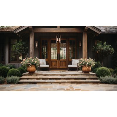 the front entrance of a house with two chairs and flowers in large planters on the steps