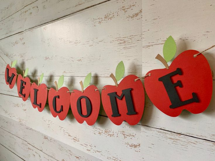 a welcome sign hanging from the side of a wall with an apple and leaves on it