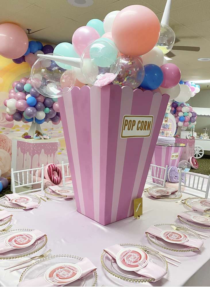 a pink and white striped popcorn box filled with balloons on a table at a birthday party